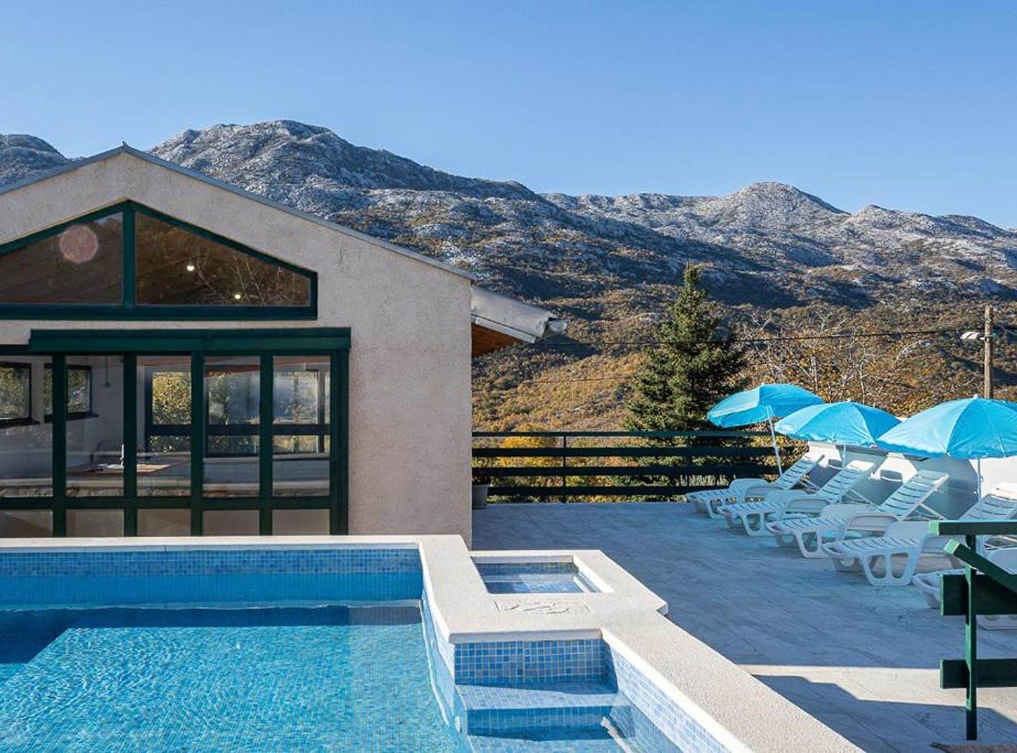 Ein Poolbereich mit Bergblick, Liegestühlen und Sonnenschirmen.
