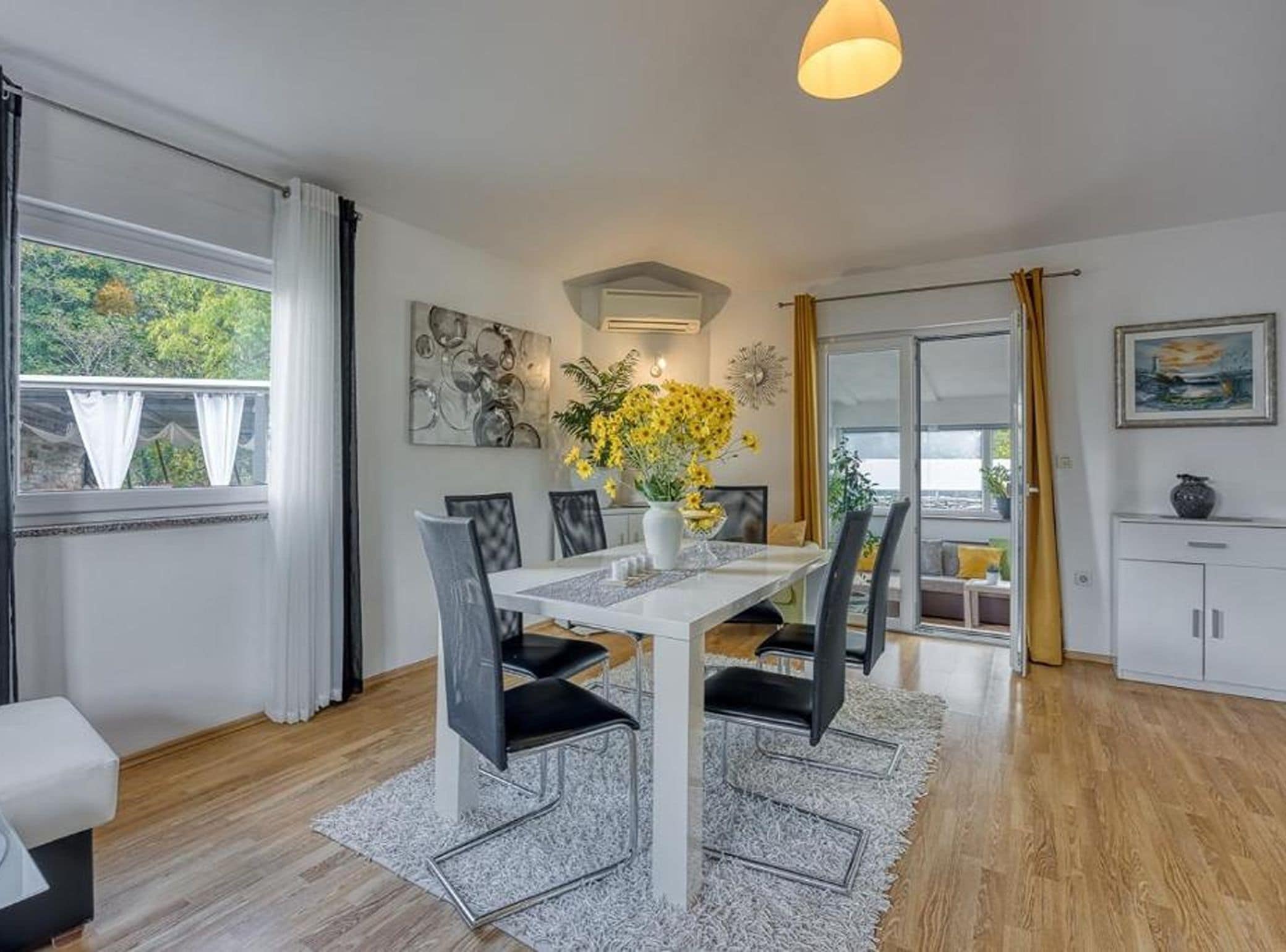 Een moderne eethoek met een witte tafel, zwarte stoelen en een vaas met gele bloemen.