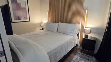 Ein Hotelzimmer mit Bett, Nachttischlampen, Teppich, Holz-Kopfteil, gerahmtem Bild an der Wand und einem kleinen Nachtkästchen.