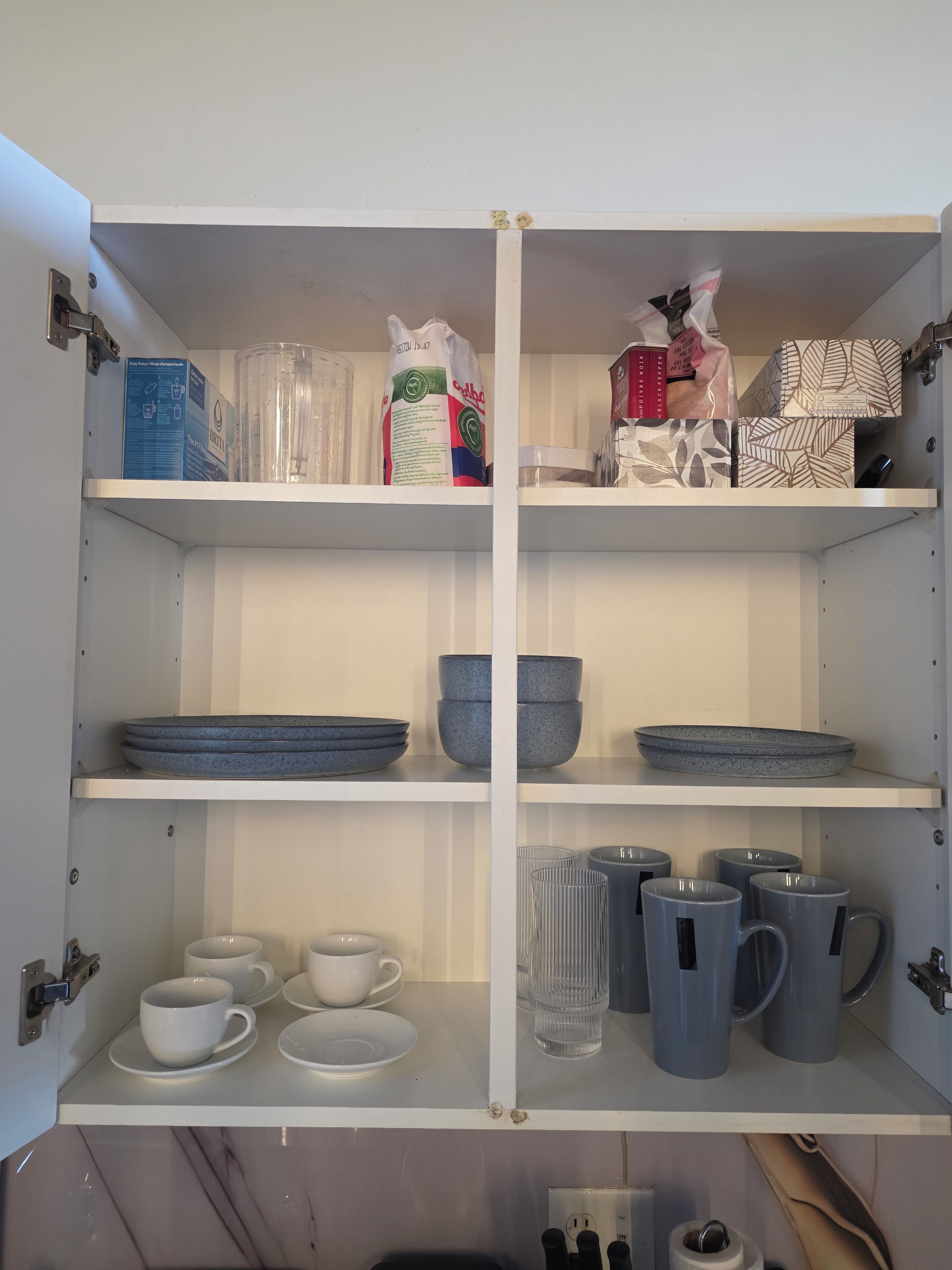 A kitchen cabinet with shelves containing various kitchenware, including plates, bowls, cups, and mugs.
