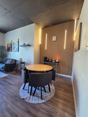 A modern living room with a round wooden table, dark sofas, and a patterned rug. - Cozy 16th-Floor Downtown Loft | City Views | Steps to ICE District (Edmonton)