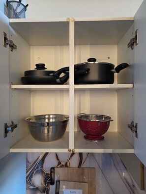 Ein Küchenschrank mit zwei Regalen, auf jedem ein Topf und ein Sieb.