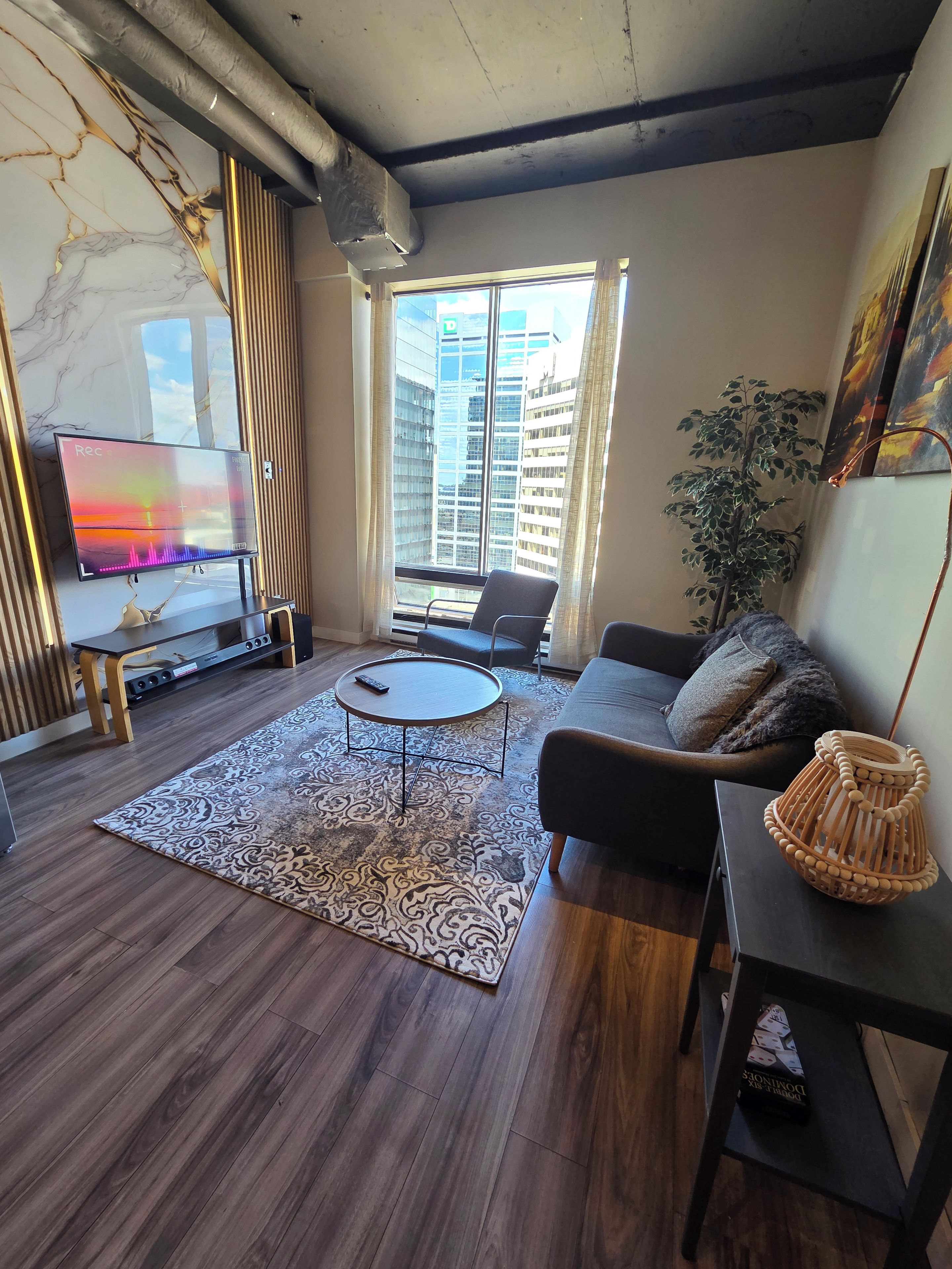 A modern living room with a marble wall, a flat-screen TV, a sofa, a coffee table, and a large window with a city view.