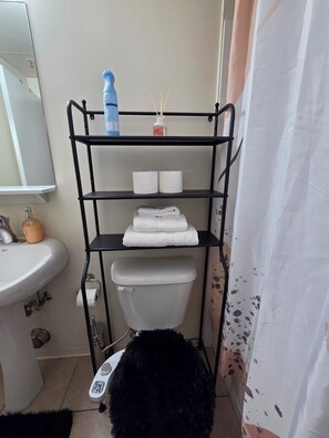 A bathroom with a black metal shelf holding toiletries, a white sink, and a toilet. - Cozy 16th-Floor Downtown Loft | City Views | Steps to ICE District (Edmonton)