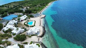 An aerial view of a coastal resort with multiple white buildings, a swimming pool, and a rocky shoreline. - New Listing (Marigot)