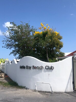 Un mur blanc sur lequel on peut lire le texte « Nettle Bay Beach Club », et un palmier aux fleurs jaunes.