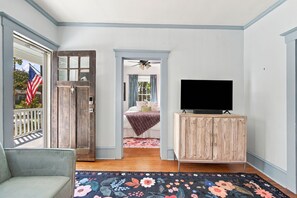 A room with a bed, a television on a wooden cabinet, a door with a window, and a flag. - Charming 1920s Cargo District bungalow! Dog friendly & near downtown Wilmington (Wilmington)