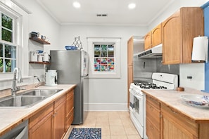 A modern kitchen with stainless steel appliances, wooden cabinets, and a window with colorful artwork. - Charming 1920s Cargo District bungalow! Dog friendly & near downtown Wilmington (Wilmington)