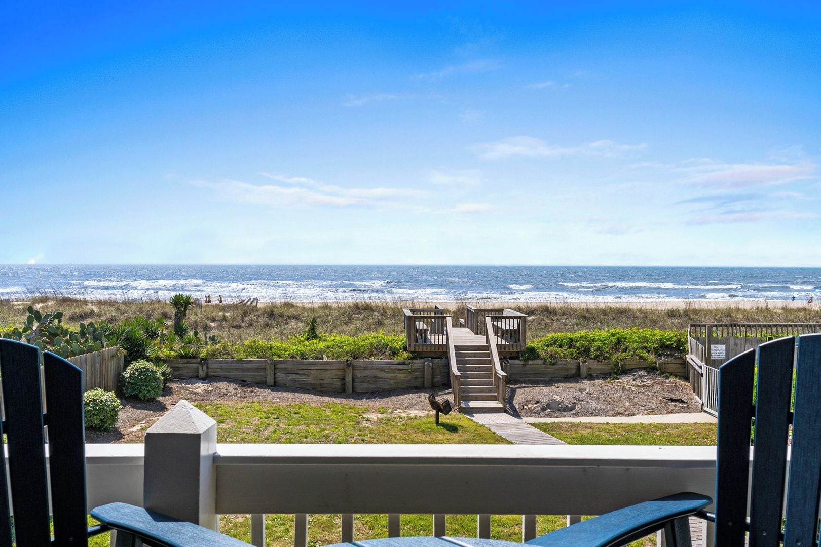 A view of a beach from a wooden deck with a staircase leading to a gazebo.