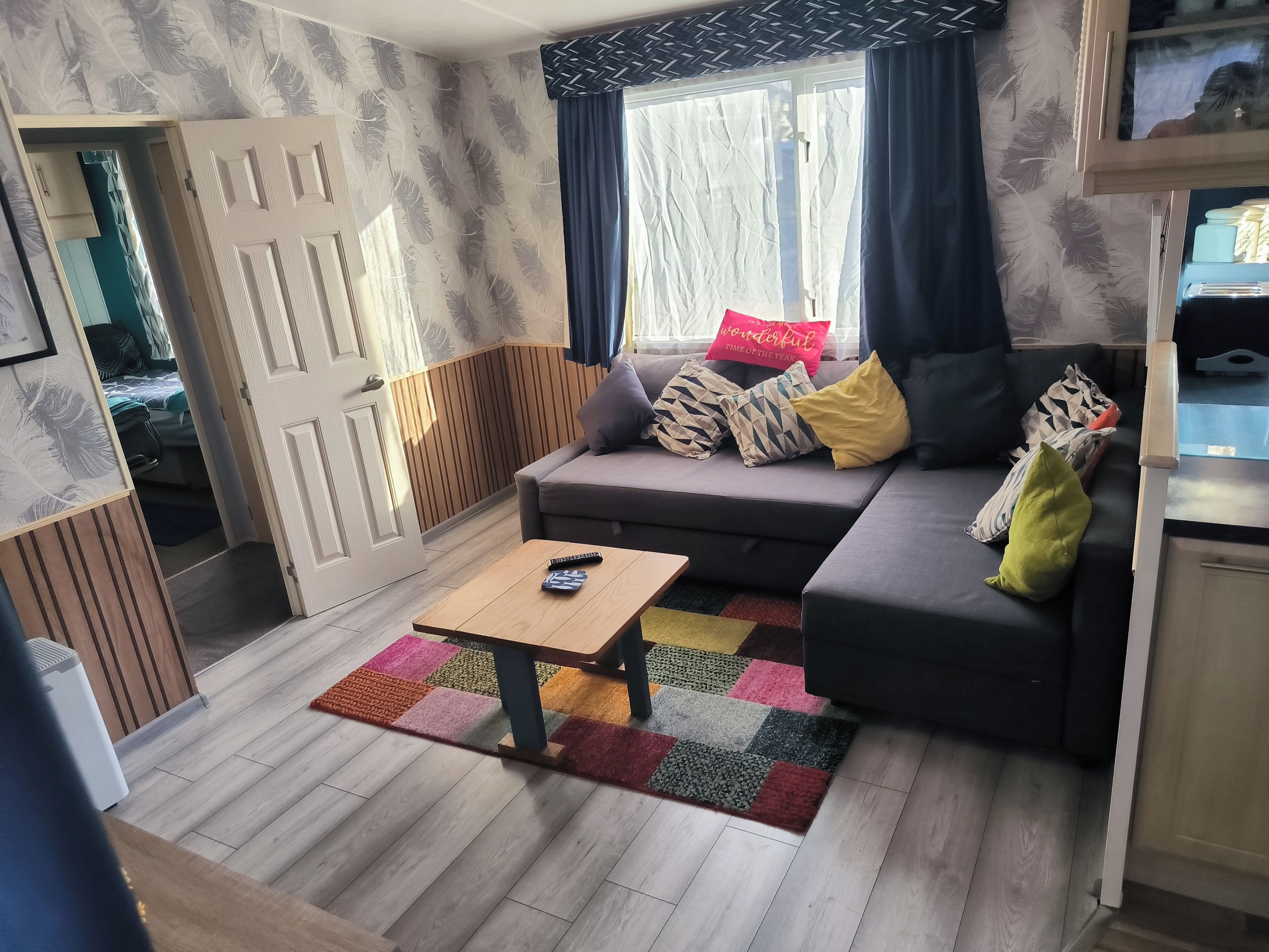 Una sala de estar con sofá, mesa de centro, alfombra y ventana con cortinas.
