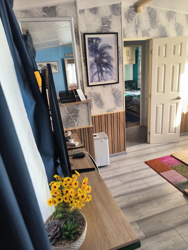 A room with a desk, a potted plant, a framed picture on the wall, and a door leading to another room.