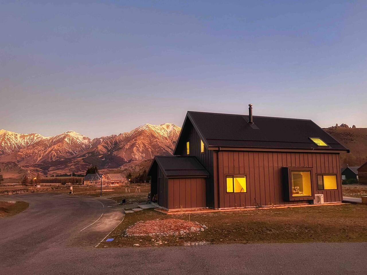 Une cabane en bois à deux étages, dotée d’une grande fenêtre et d’une cheminée, se dressant sur un fond de montagnes.