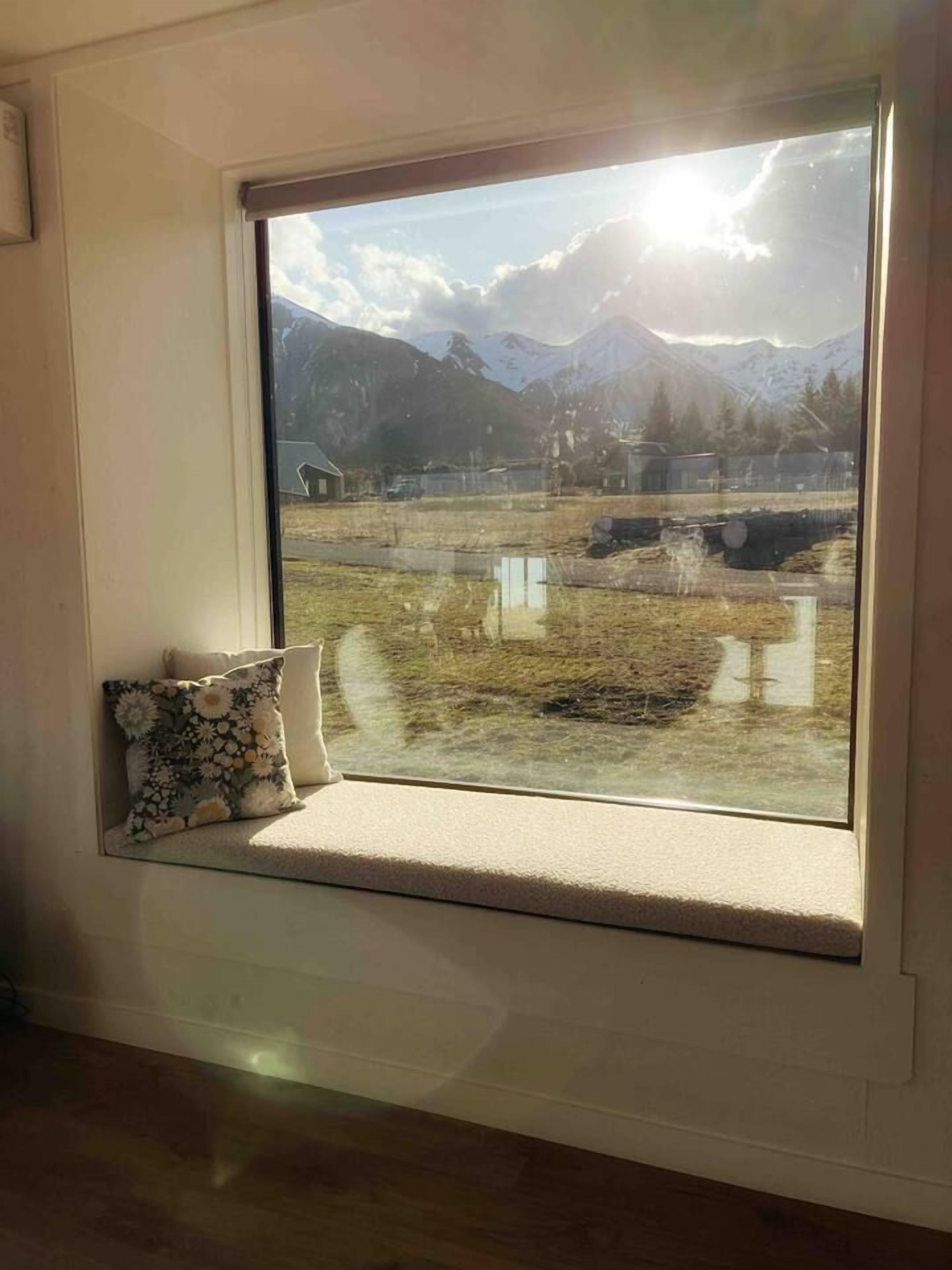 A window with a view of a mountainous landscape, a cushion, and a small ledge.