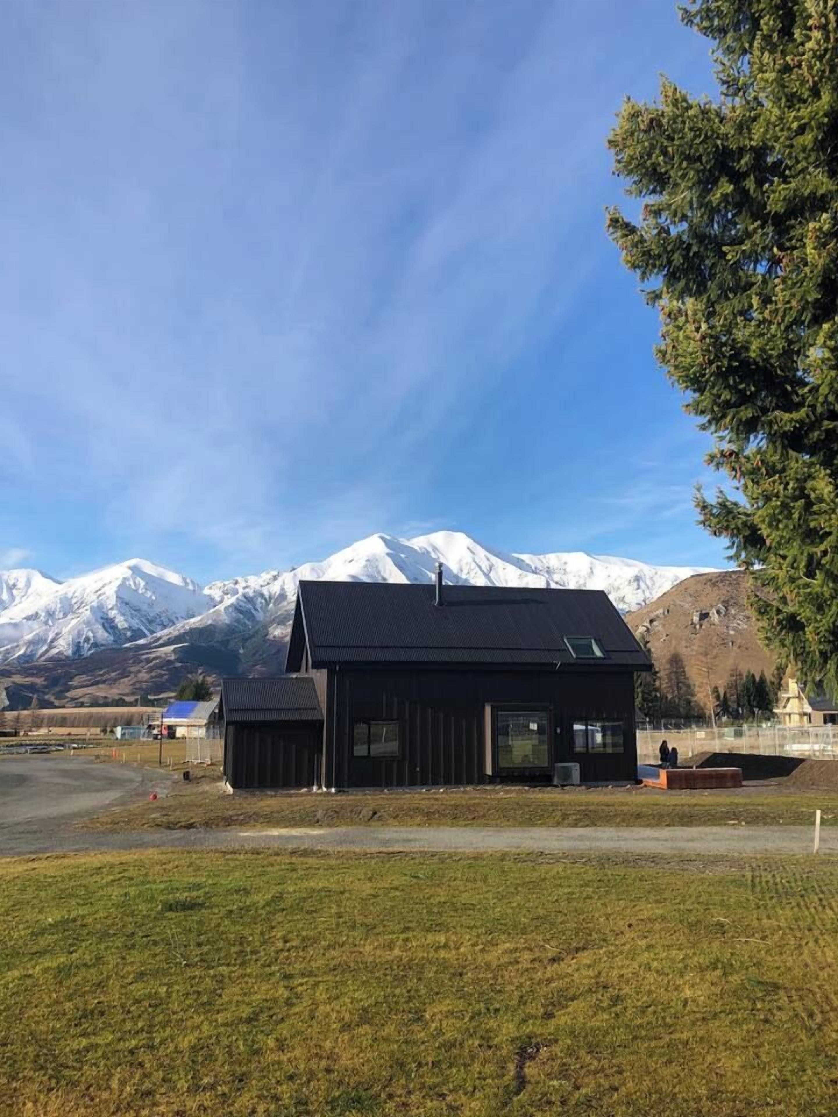 A modern building with a sloped roof, large windows, and a view of snow-capped mountains in the background.