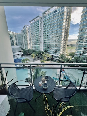 A balcony with a view of a swimming pool, palm trees, and high-rise buildings. - Cinematic Playhouse @Azure,Beach View w/ PS5 (Parañaque)