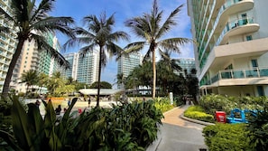 A hotel courtyard with palm trees, a pool, and modern buildings in the background. - Cinematic Playhouse @Azure,Beach View w/ PS5 (Parañaque)