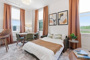Ein Hotelzimmer mit einem Bett, einem Schreibtisch mit Stühlen, einem kleinen Tisch mit einer Pflanze und Bildern an der Wand.