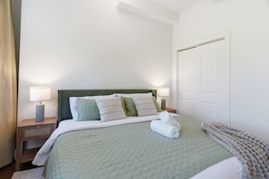A neatly made bed with a green headboard, white bedding, and a rolled towel on the side. There are two bedside tables with lamps and a small rug. - DWTN I King Bed I Free Parking I Green View I Gym (New Haven)