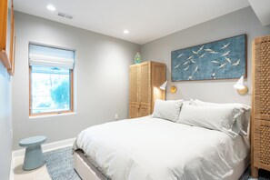Un dormitorio con cama, ventana con persianas, lámpara de pared y una obra de arte en la pared.