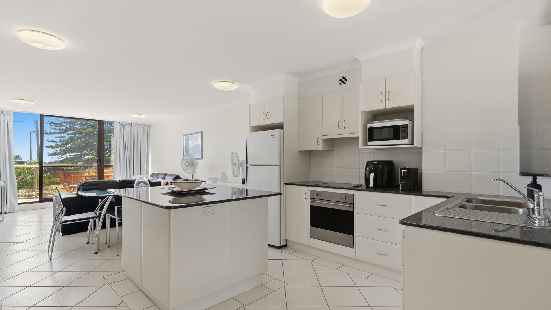 Een moderne keuken met witte kasten, een centraal eiland en uitzicht op het buiten.