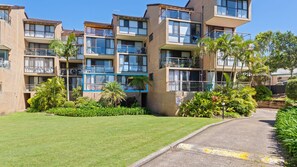A multi-story residential building with balconies, a well-maintained lawn, and a paved driveway. - Unit 53 Beachpark Apartments (Port Macquarie)