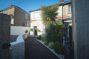 A narrow residential street with houses on both sides, a paved path, and a variety of plants and shrubs. - Beautiful House 5 Mins Walk Into Ulverston (Ulverston)