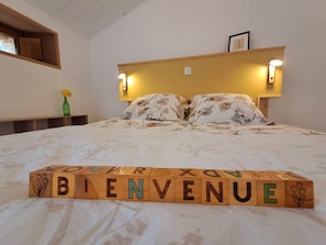 Una cama con ropa de cama floral y un bloque de madera que dice 'BIENVENUE'.