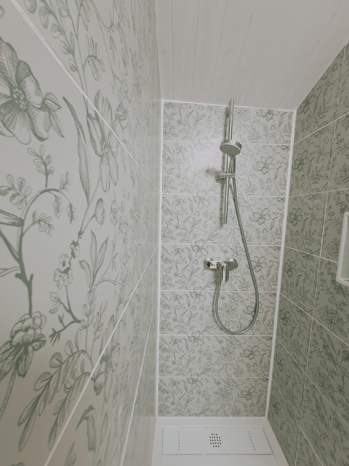 Een douche met een patroon van bloementegels op de wanden en een douchekop.