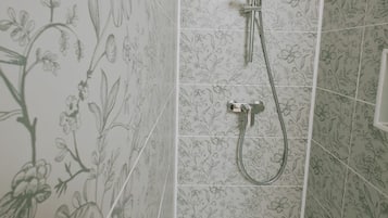 Een douche met een patroon van bloementegels op de wanden en een douchekop.