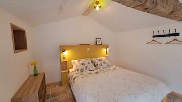 Een slaapkamer met een bed, nachtkastje, een wandlamp, houten hoofdbord, een klein plankje met een vaas en een kapstok.