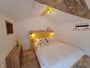 A bedroom with a bed, a nightstand, a wall-mounted light, a wooden headboard, a small shelf with a vase, and a coat rack. - New Listing (Voulmentin)