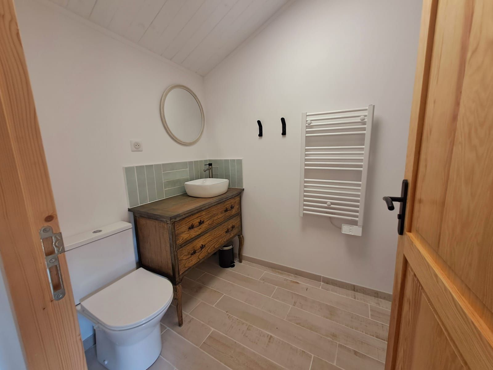 Une salle de bain comprenant des toilettes, un meuble-lavabo en bois avec un évier, un miroir et un porte-serviettes.