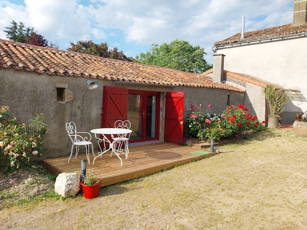 A rustic building with a tiled roof, a wooden deck, and a red door.