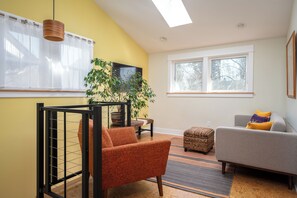 A living room with a sofa, armchair, and a TV on the wall. - Dragonfly Cottage in lovely Kern's neighborhood. Safe, walkable, fun! (Portland)