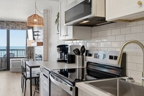 A modern kitchen with white cabinets, a stainless steel sink, and a large window overlooking a balcony. - Beachfront Condo with Pools and Hot tubs (Myrtle Beach)