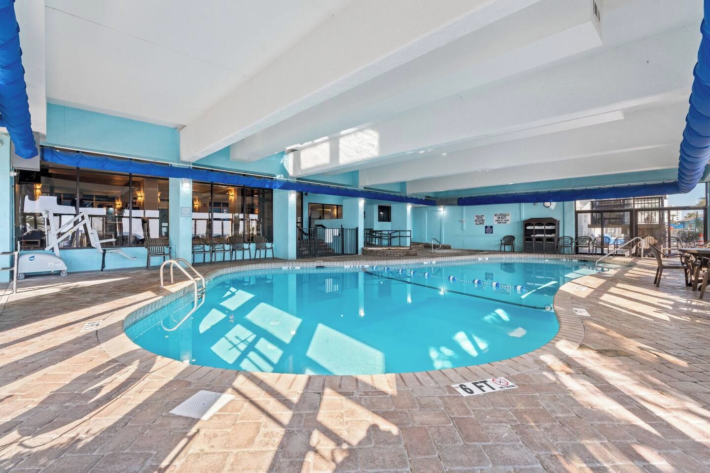 Ein Hallenbad mit gefliestem Deck, einer Rettungswache und einem Sitzbereich mit Stühlen.