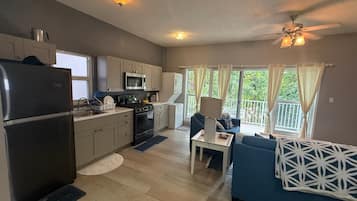 Een compacte keuken met moderne apparaten, een zithoek met een blauwe bank en een balkon met gordijnen.