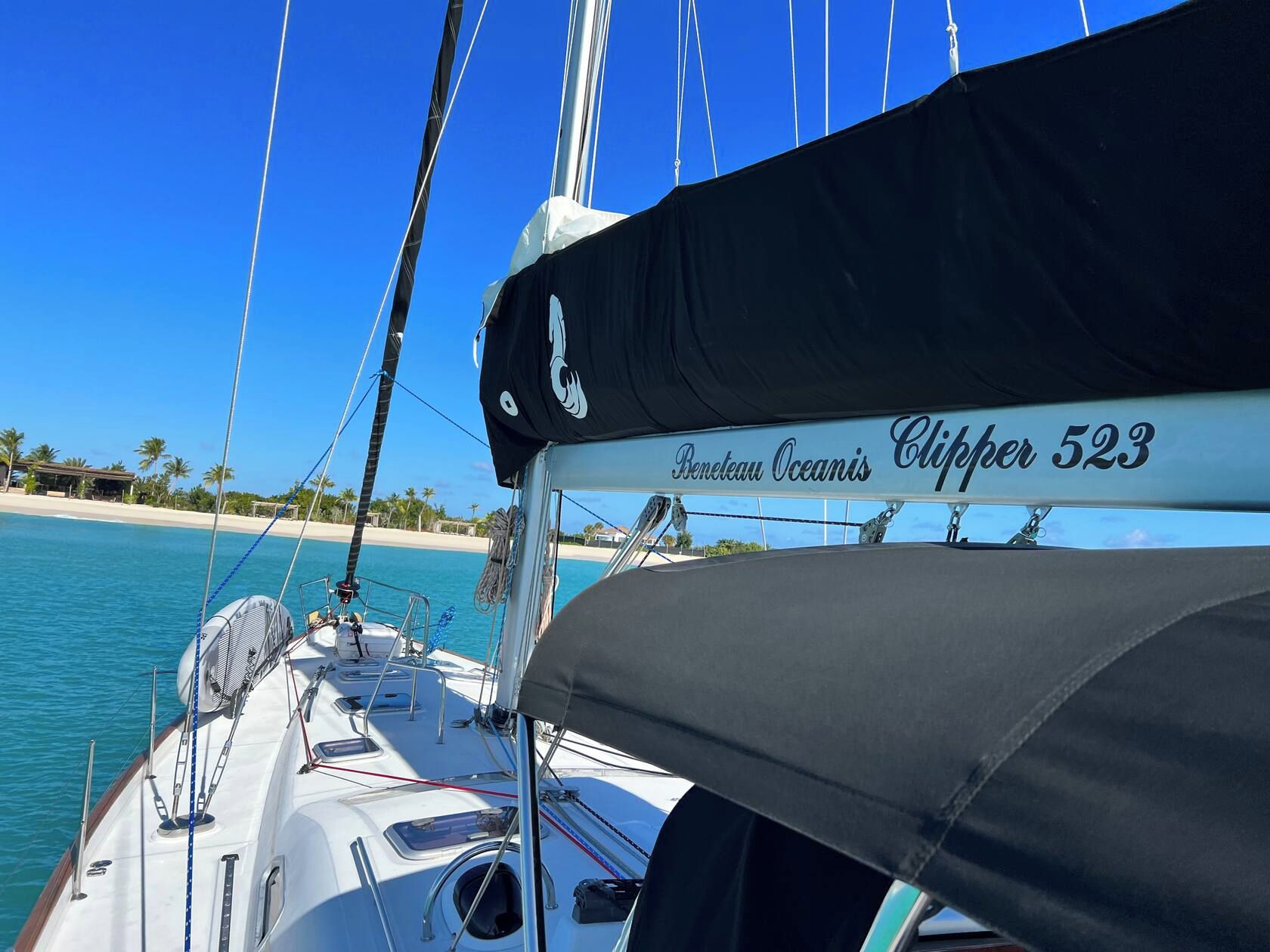 A sailboat with a name 'Beneteau Oceanis Clipper 523' and a beach with palm trees in the background.