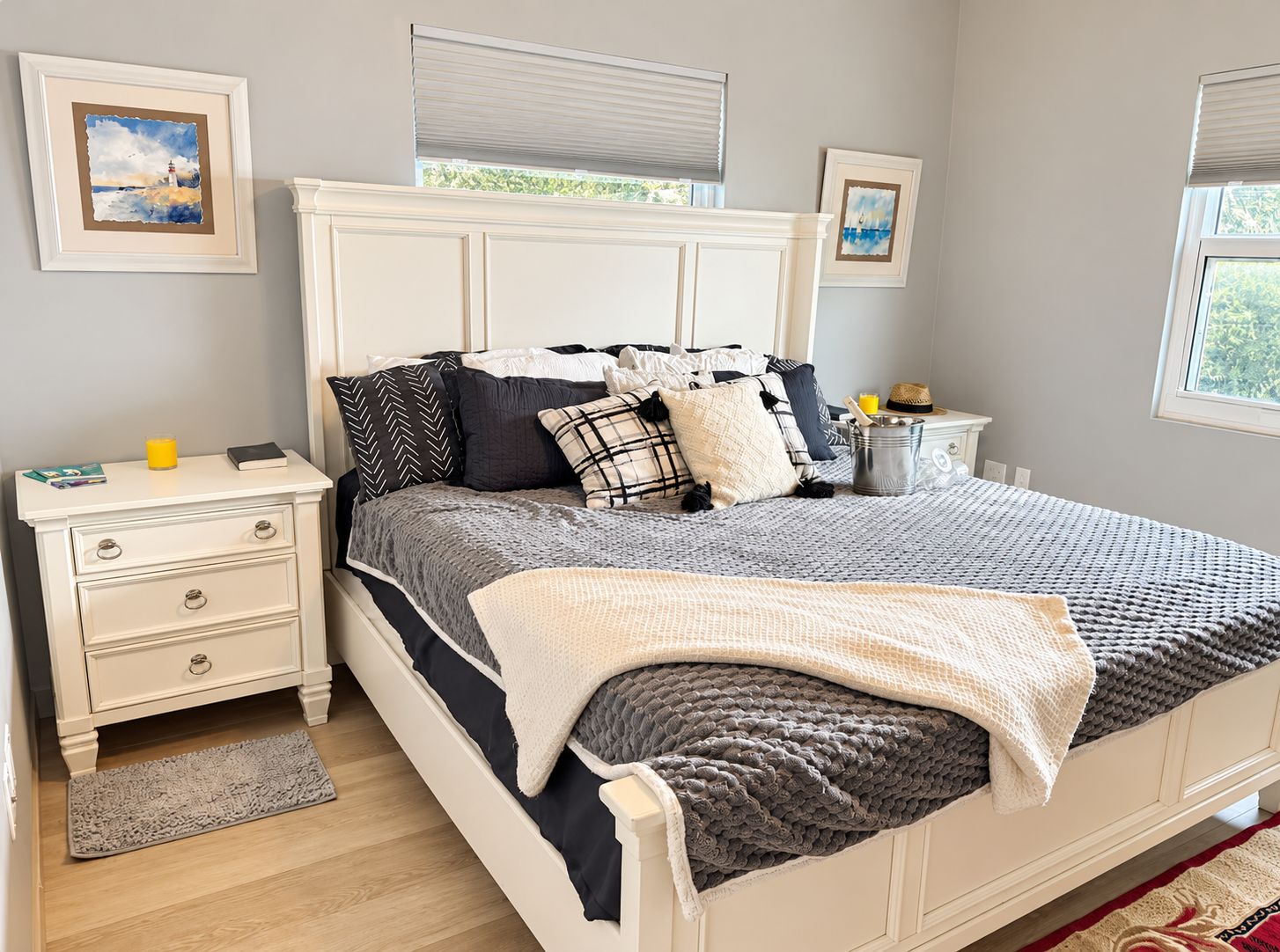 A bedroom with a bed, bedside tables, a nightstand, a window with blinds, and artwork on the walls.