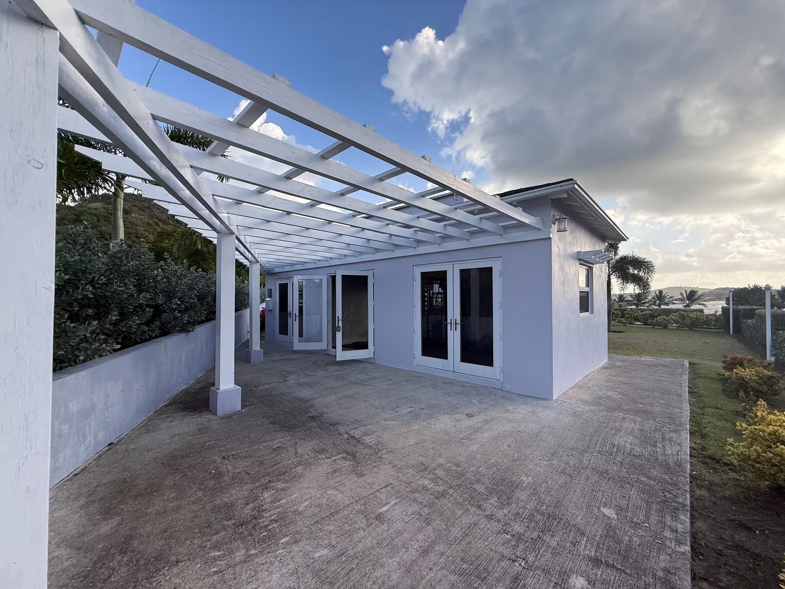 A covered outdoor area with a concrete floor, white walls, and a glass door entrance.