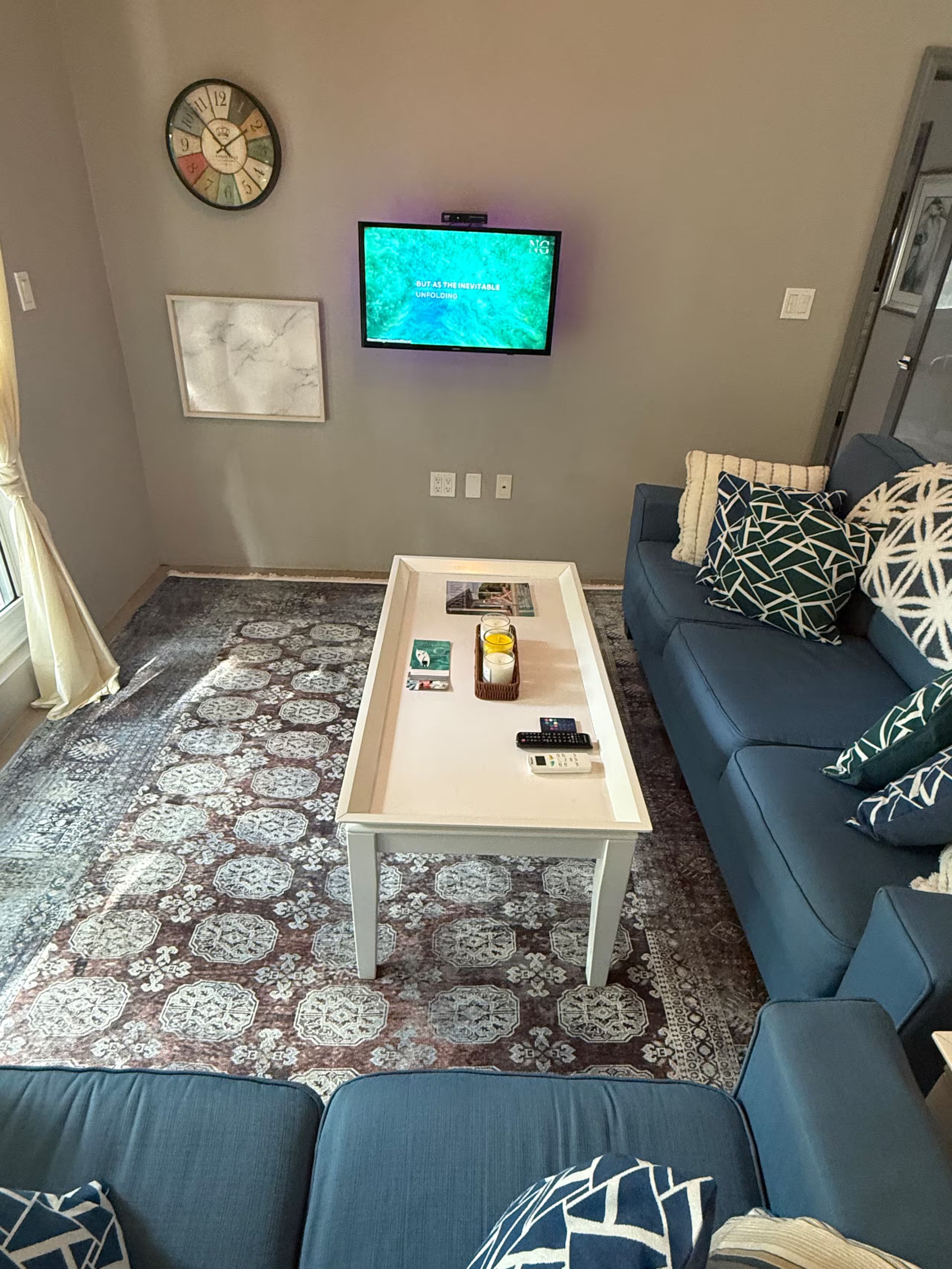 A living room with a sofa, a coffee table, a television, and a patterned rug.
