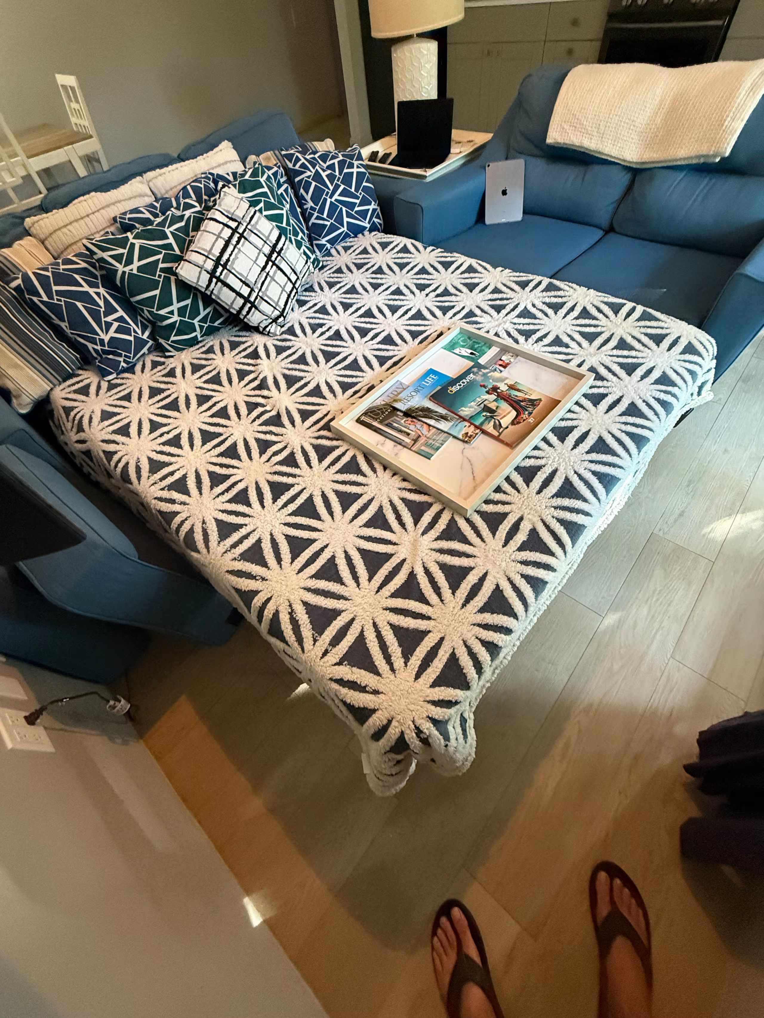 A bed with a geometric patterned bedspread, a laptop on a side table, and a magazine on the bed.