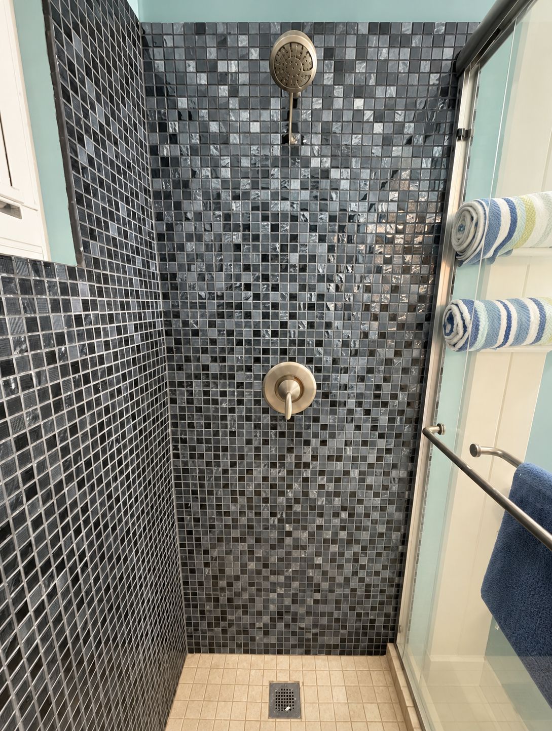 En dusch med en kaklad vägg, ett duschmunstycke och en handdukshängare med handdukar.