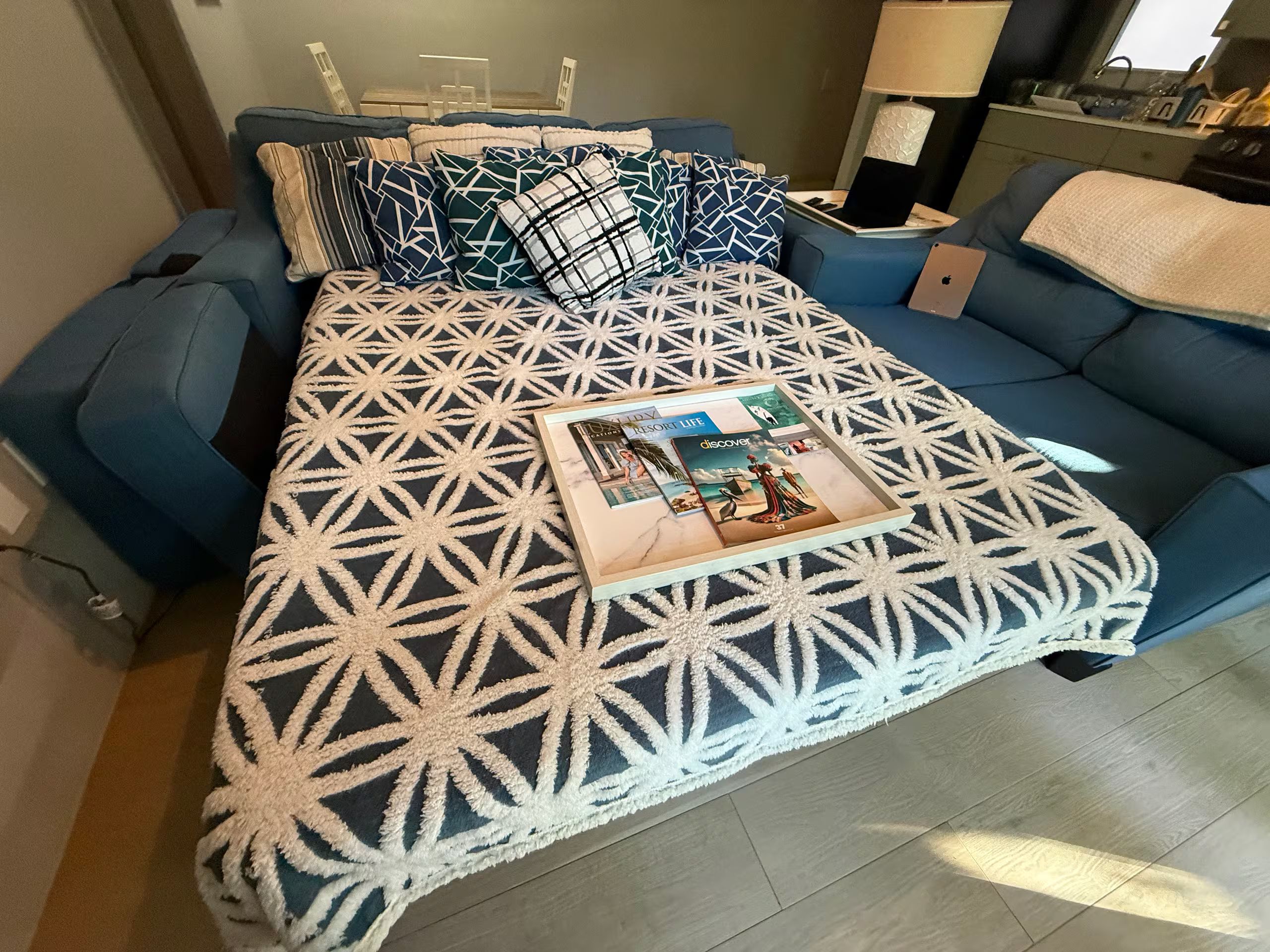 A bed with a geometric patterned bedspread, a pillow with a similar pattern, and a magazine on the bed.