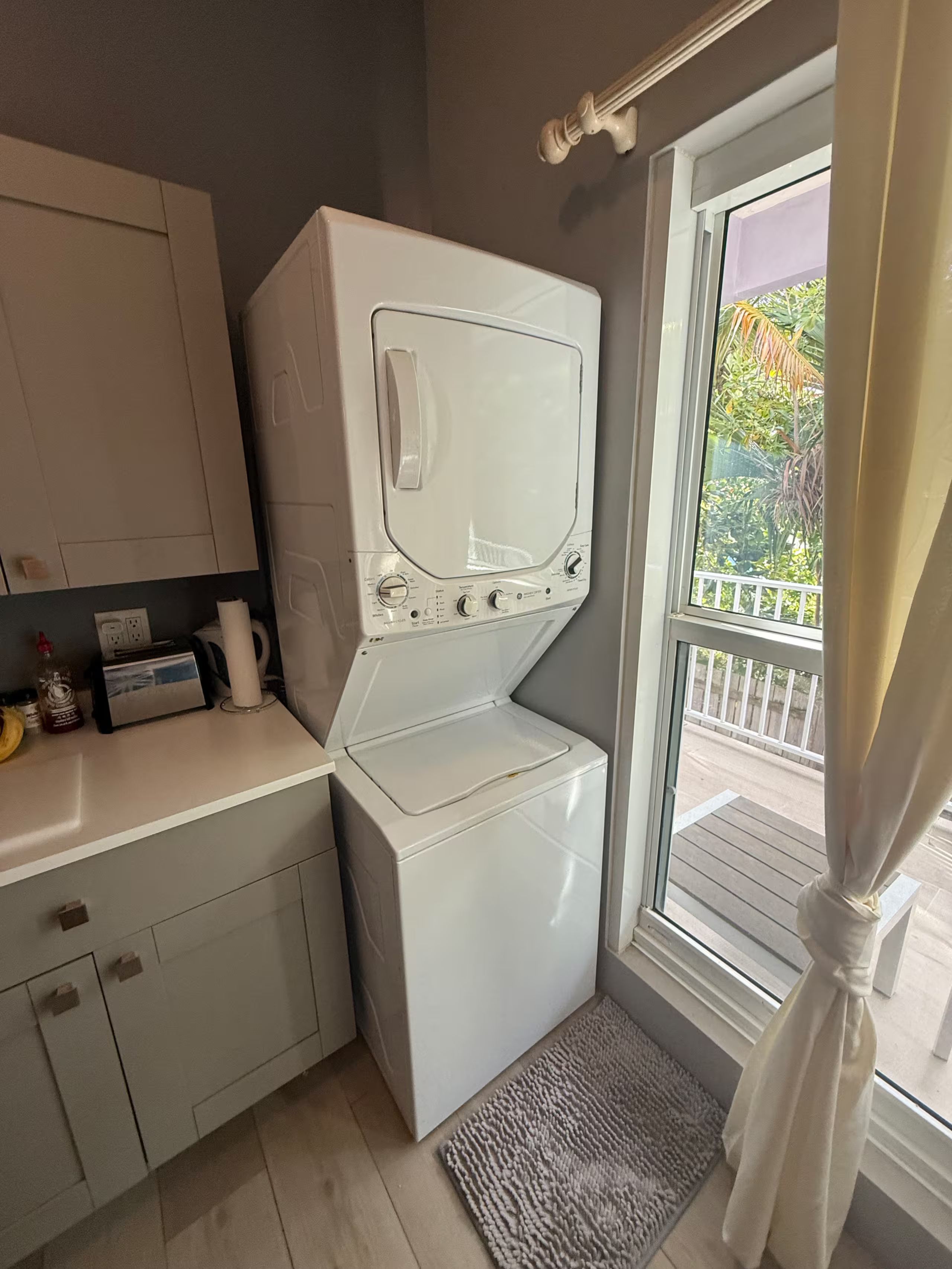 A laundry room with a front-loading washer and dryer, a countertop with a few items, and a view of the outside through a window.