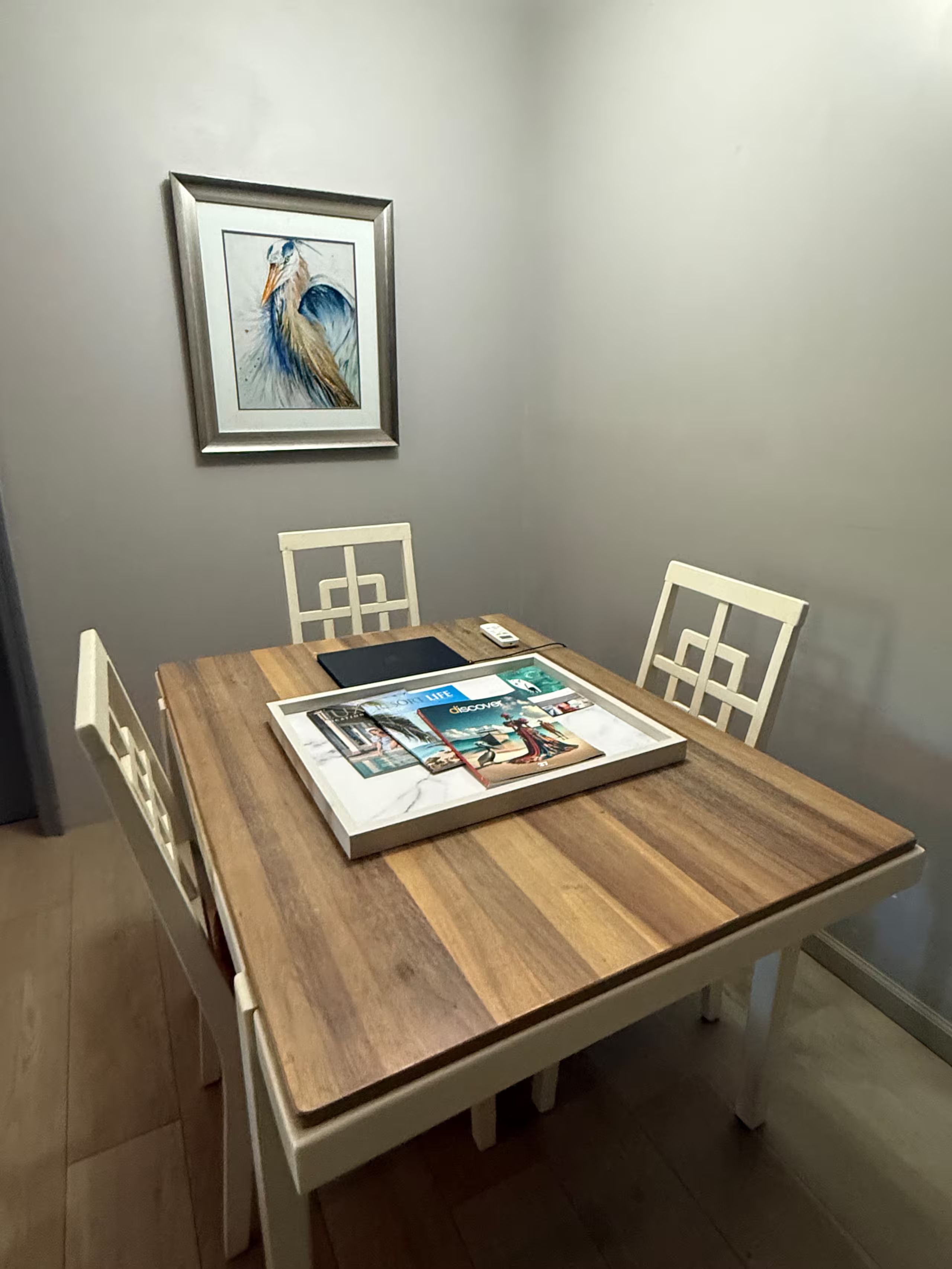 Een eettafel met een lijstwerk kunstwerk erboven, omringd door witte stoelen.