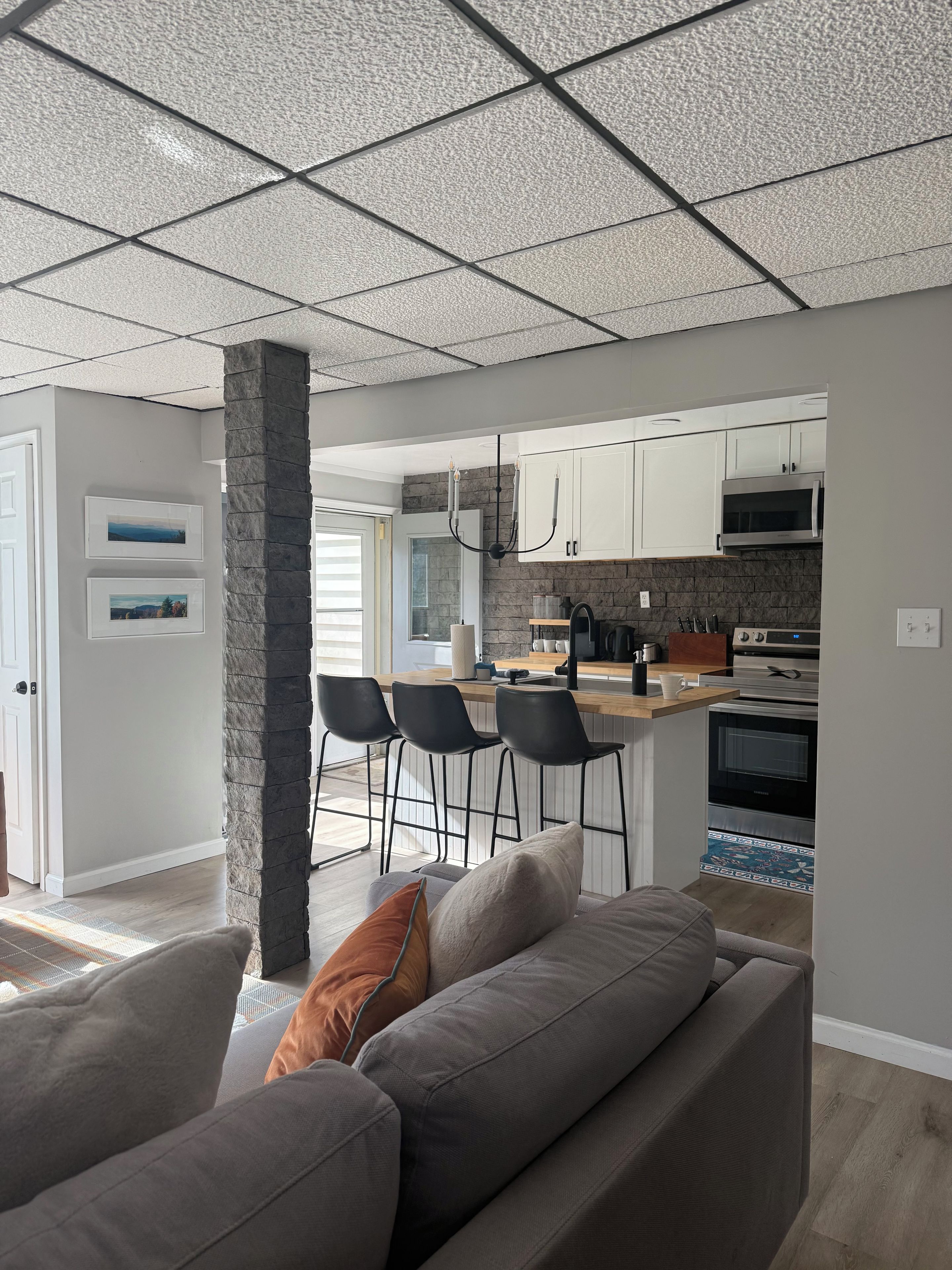 A modern kitchen with white cabinets, a microwave, and an oven. There is a bar area with stools and a countertop.