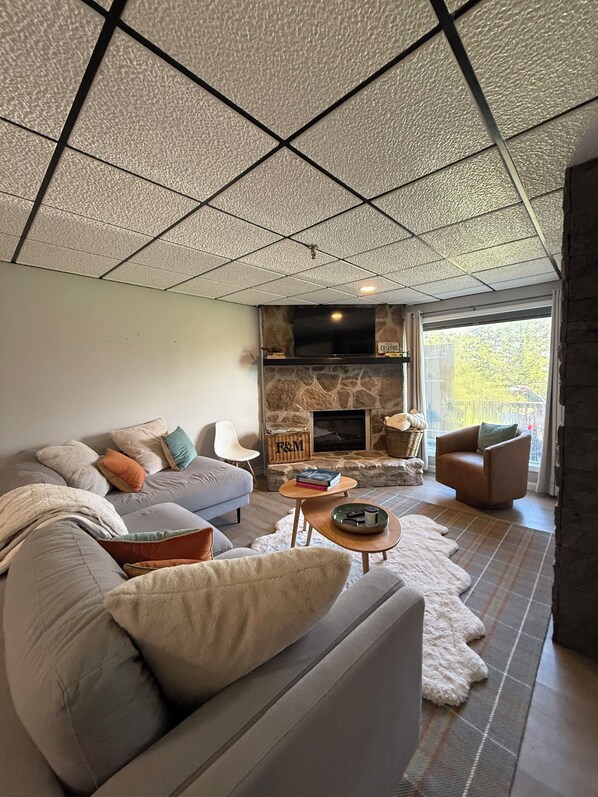 Una sala moderna con chimenea de piedra, un conjunto de sofás, un televisor y un ventanal grande.