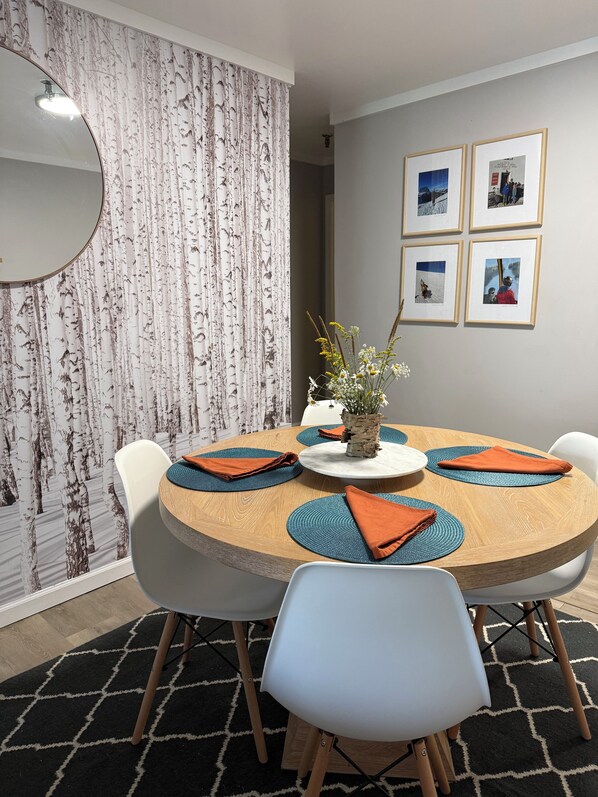 A dining area with a round table, white chairs, and orange placemats. - Your Perfect Snowshoe  Getaway make most of the mountains in this stylish condo! (Snowshoe)