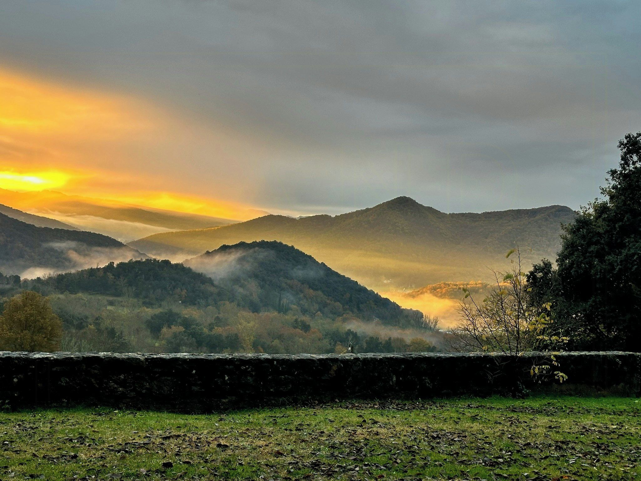 A mountainous landscape with a stone wall in the foreground.